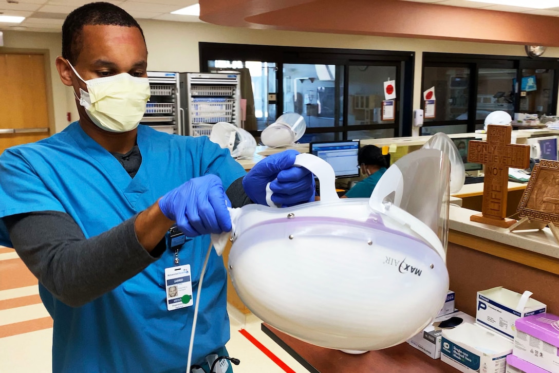 An Air Force cardiopulmonary lab technician wearing a face mask and gloves cleans his personal protective equipment after assisting a COVID-19 patient.