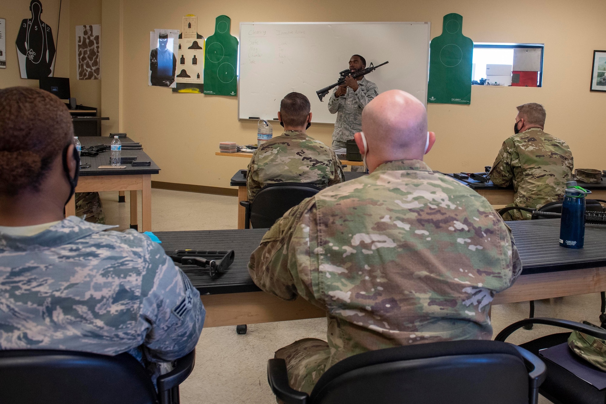 A male instructor holds up an M4 carbine in front of a class of Airmen