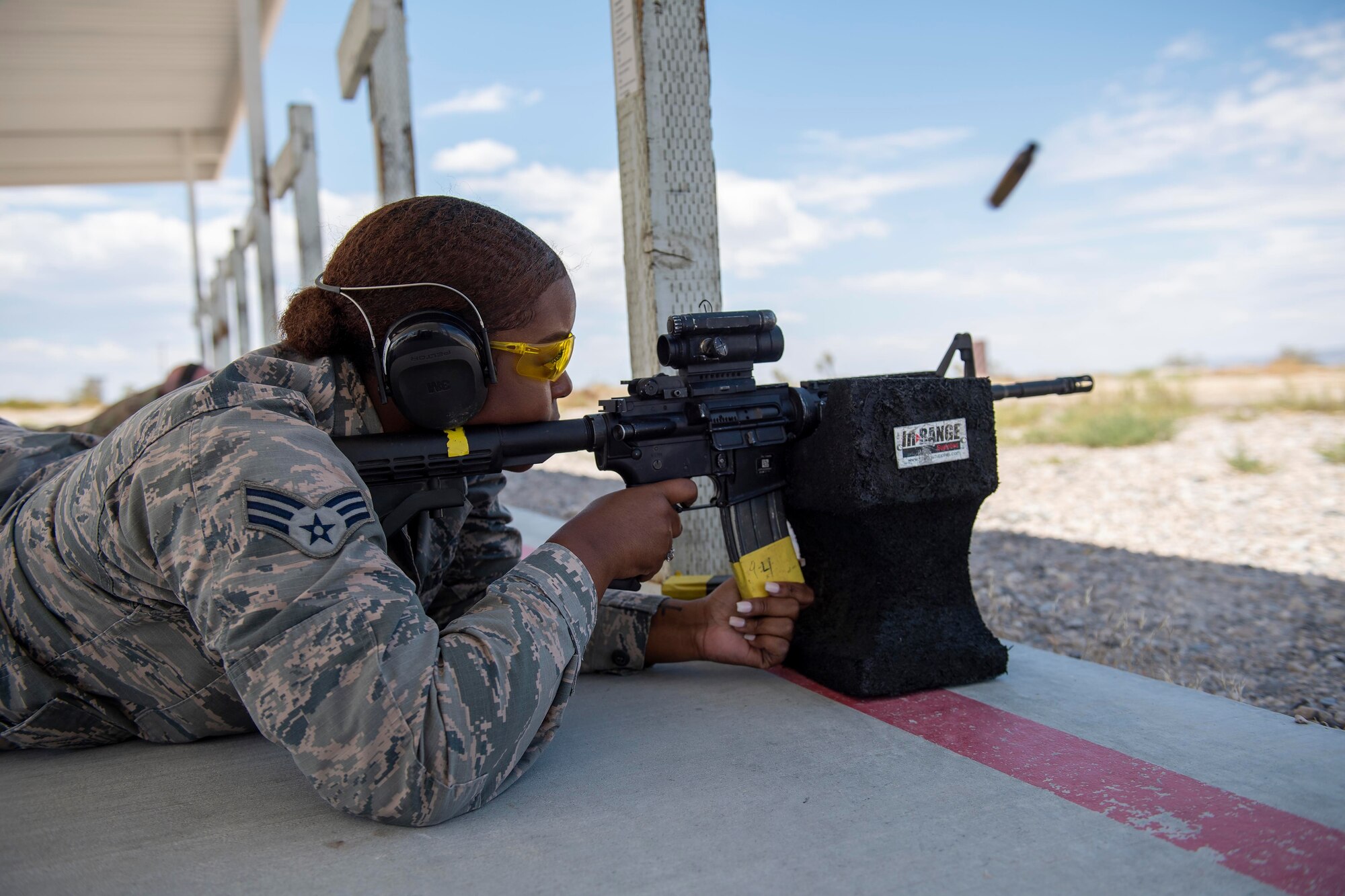 A female Airman lays in the prone position while firing an M4 carbine.