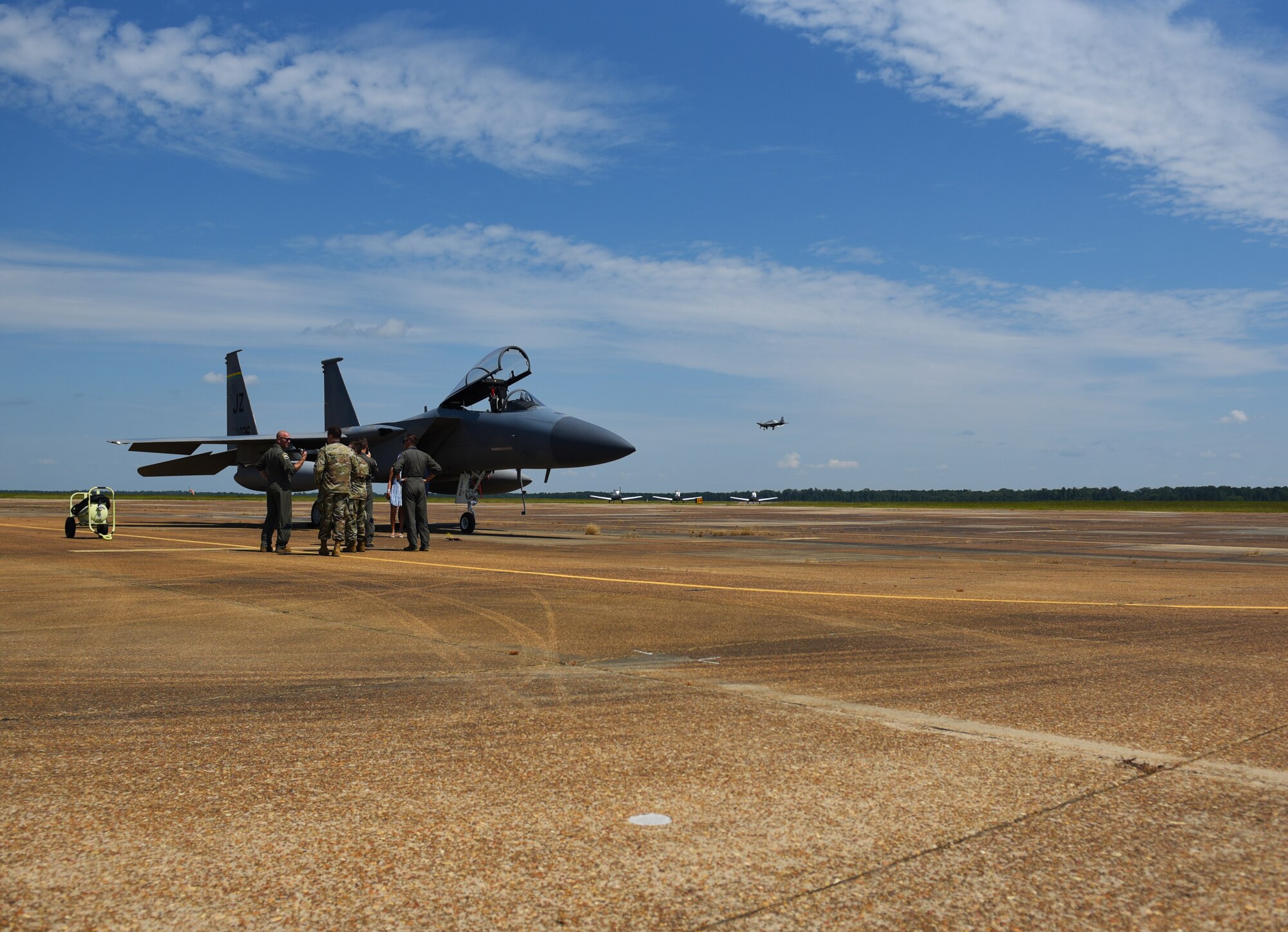 Airmen discuss with one another while an F-15 Eagle sits on the flightline with four T-6A Texan IIs in the background on August 7, 2020, at Columbus Air Force Base, Miss. The F-15 Eagle is an all-weather, extremely maneuverable, tactical fighter designed to permit the Air Force to gain and maintain air supremacy over the battlefield. (U.S. Air Force photo by Senior Airman Jake Jacobsen)