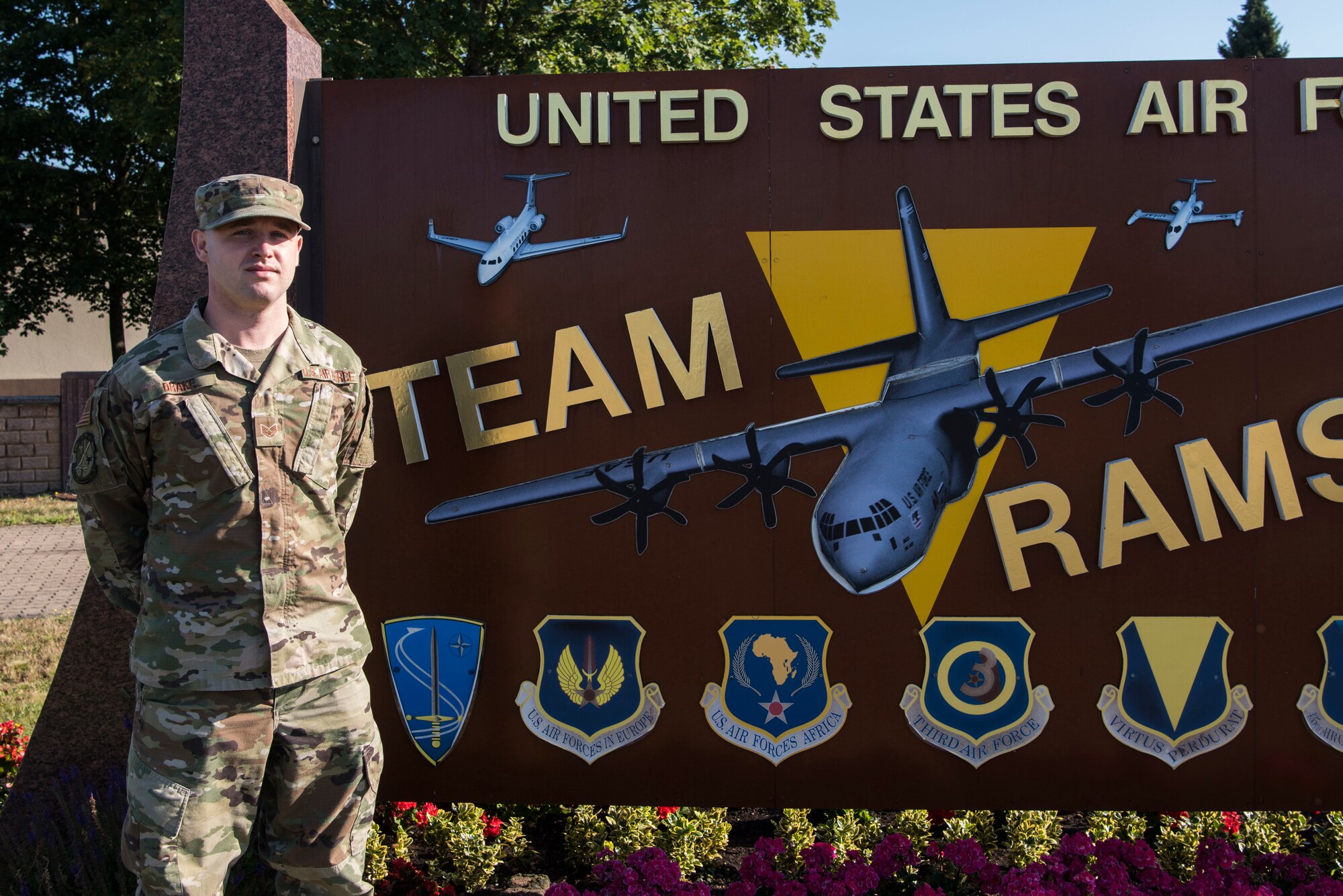 U.S. Air Force Staff Sgt. Corey Drake, 1st Combat Communications client systems technician, stands in front of a wing sign at Ramstein Air Base.