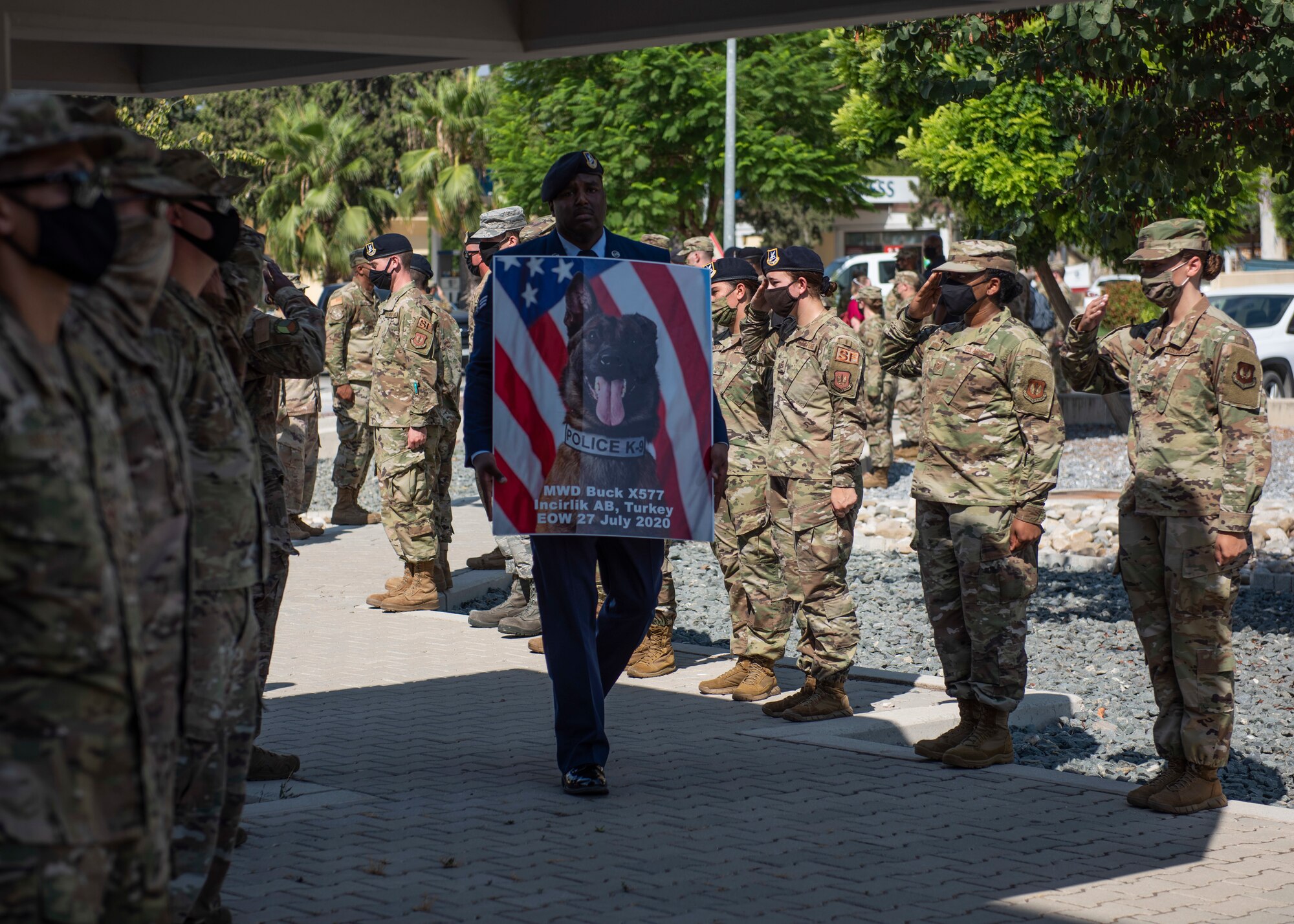 U.S. Senior Airman Antoine Carr holds a memorial poster of MWD Buck while walking past saluting SFS Airmen, Aug. 5, 2020, at Incirlik Air Base, Turkey.