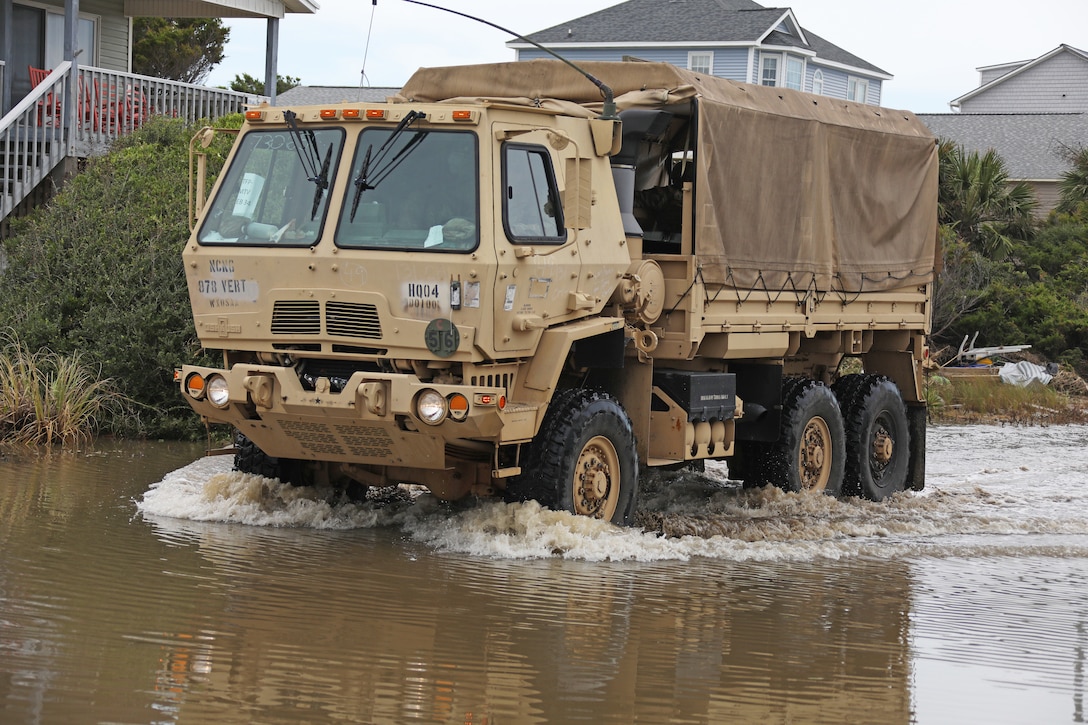 Members of the North Carolina National Guard drive vehicles assigned to the 878th Engineer Vertical Construction Company, 105th Engineer Battalion, through flooded roads to assist stranded people on Oak Island, North Carolina, Aug. 5, 2020. The NCNG deployed teams across the eastern portion of the state to help respond after Hurricane Isaias.