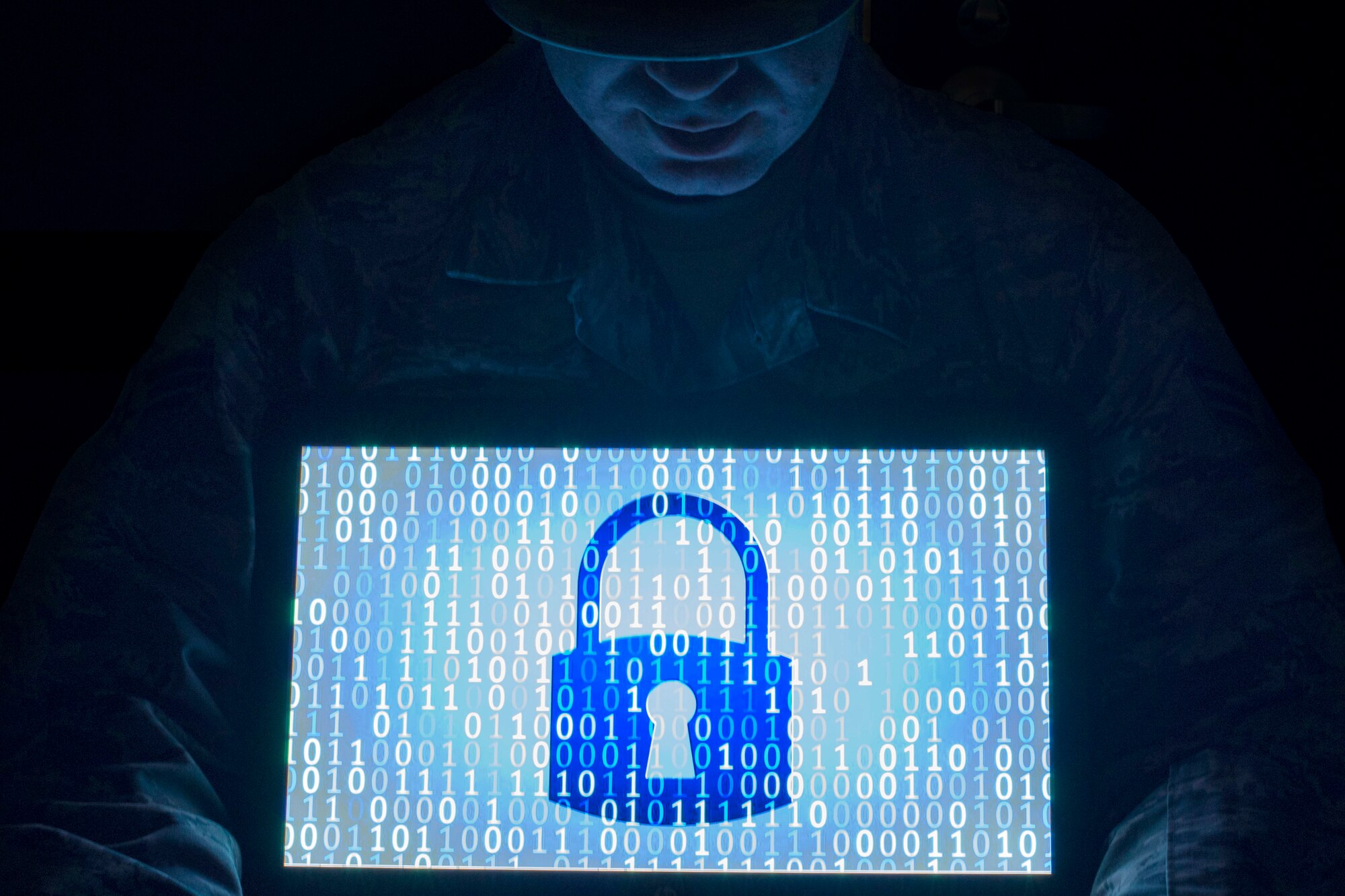 An illustration shows a man with his eyes obscured by a hat. He holds a computer screen with a padlock and zeros and ones.