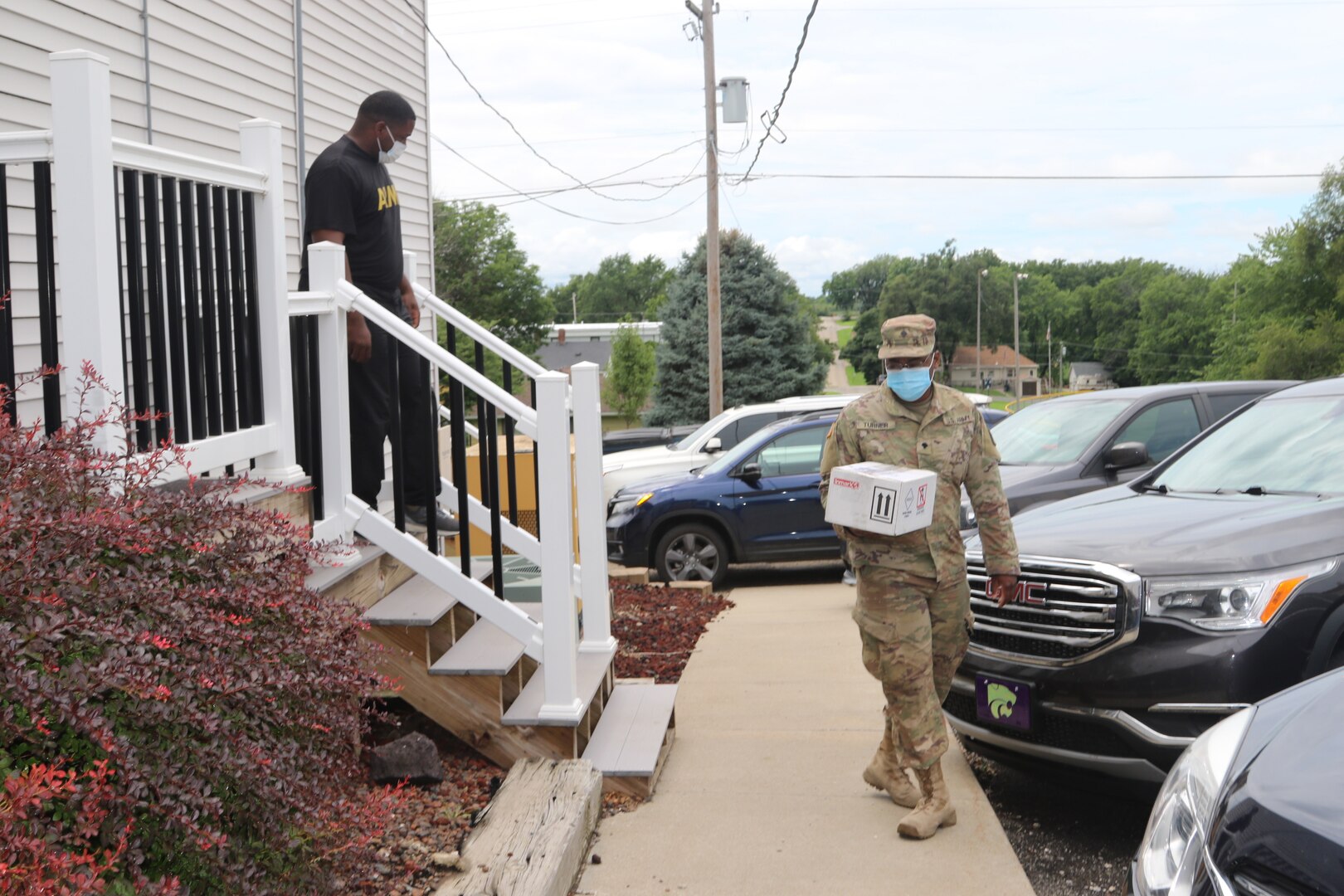 Kansas Army National Guard Staff Sgt. Raymond Owes and Spc. Adrian Turner, both with the 997th Brigade Support Battalion, taking a box of COVID-19 test samples to their vehicle in Troy, Kansas, July 27, 2020. Kansas National Guard teams have been transporting COVID-19 samples from across the state to the state health department lab since March.