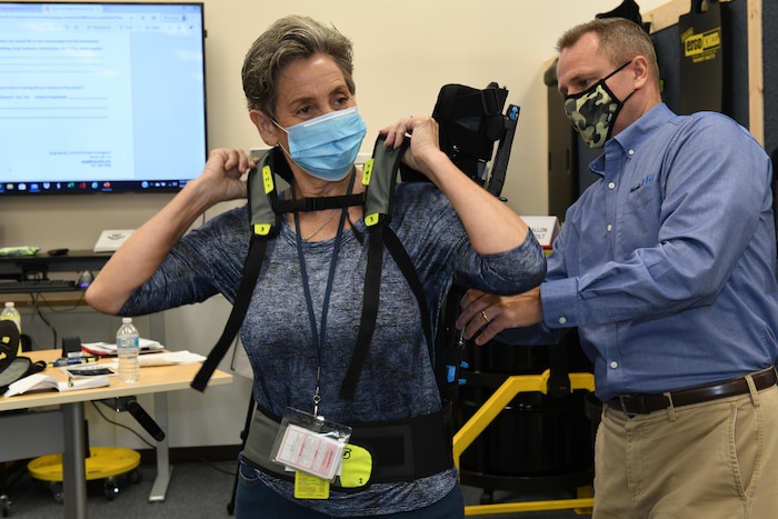 Photo shows a woman putting on an upper body exoskeleton suit.