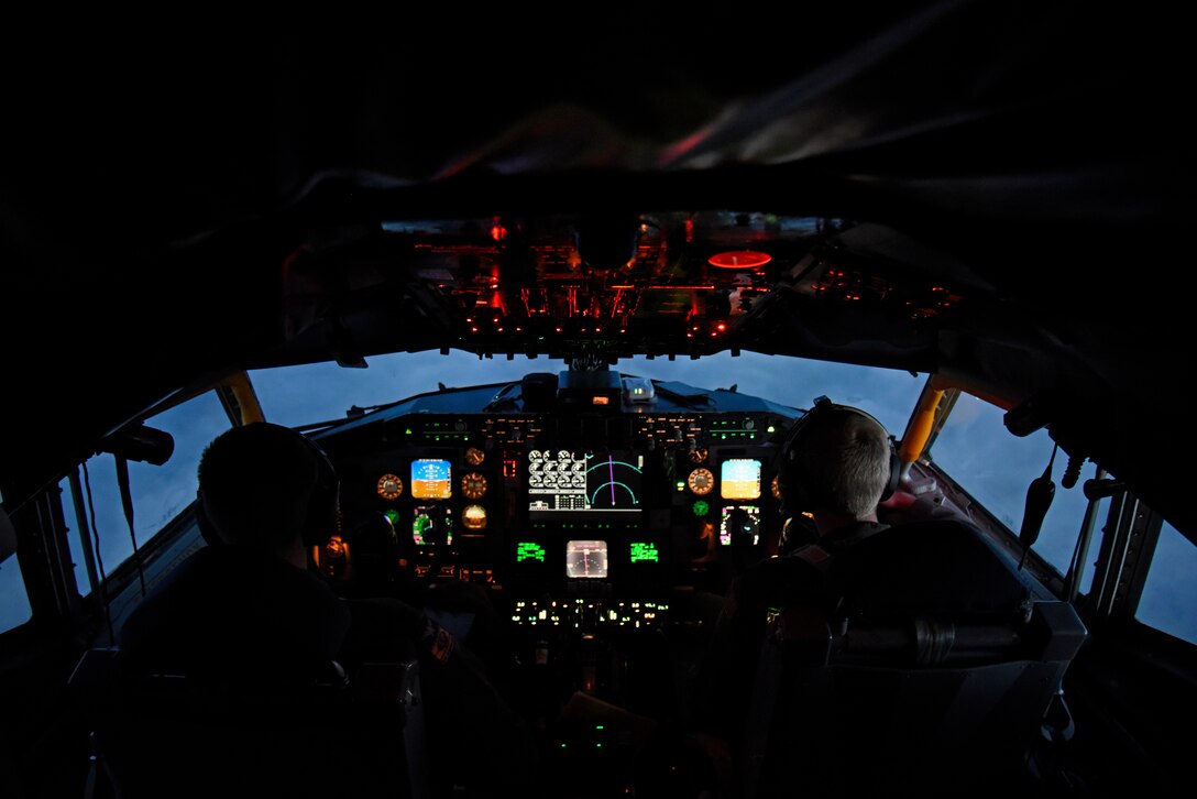 Two airmen are silhouetted as they sit in the cockpit of an aircraft.