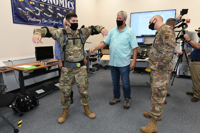 Photo shows three men with one putting on an upper body assist suit.