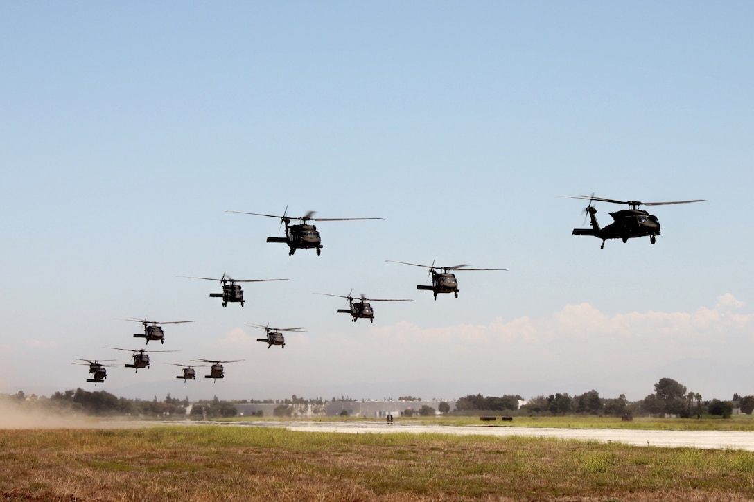 A large group of helicopters fly in formation close to the ground.