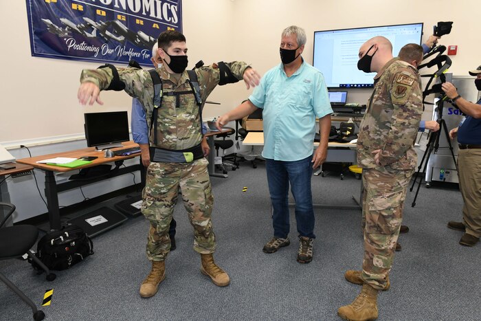 Photo shows three men with one putting on an upper body assist suit.