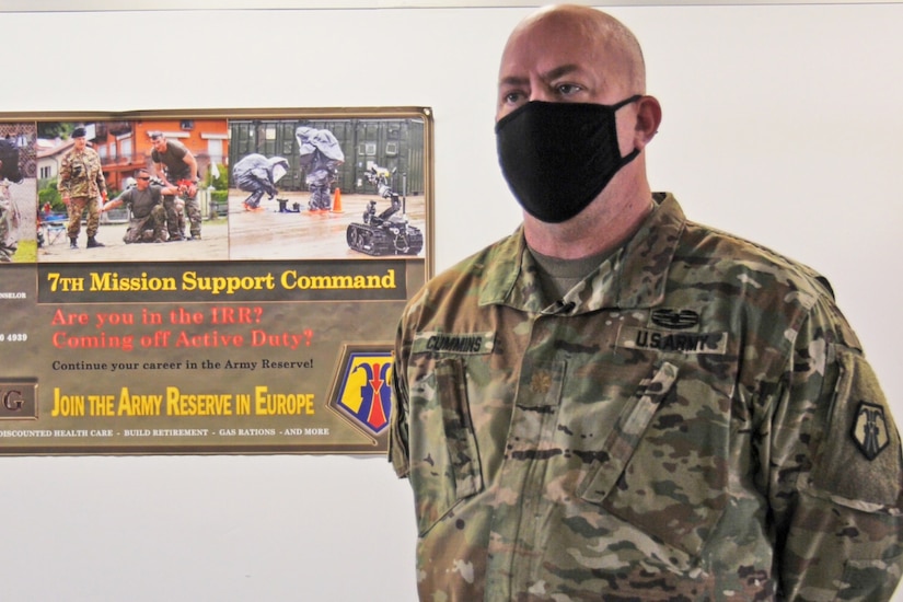 A soldier wearing a mask stands in front of a sign.