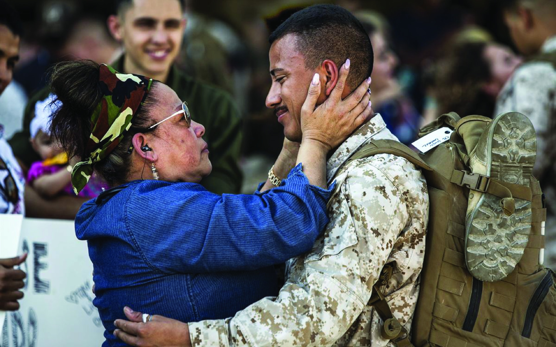 Solider and mother facing and looking at each other in welcome embrace with mother holding soldier's face in her hands.