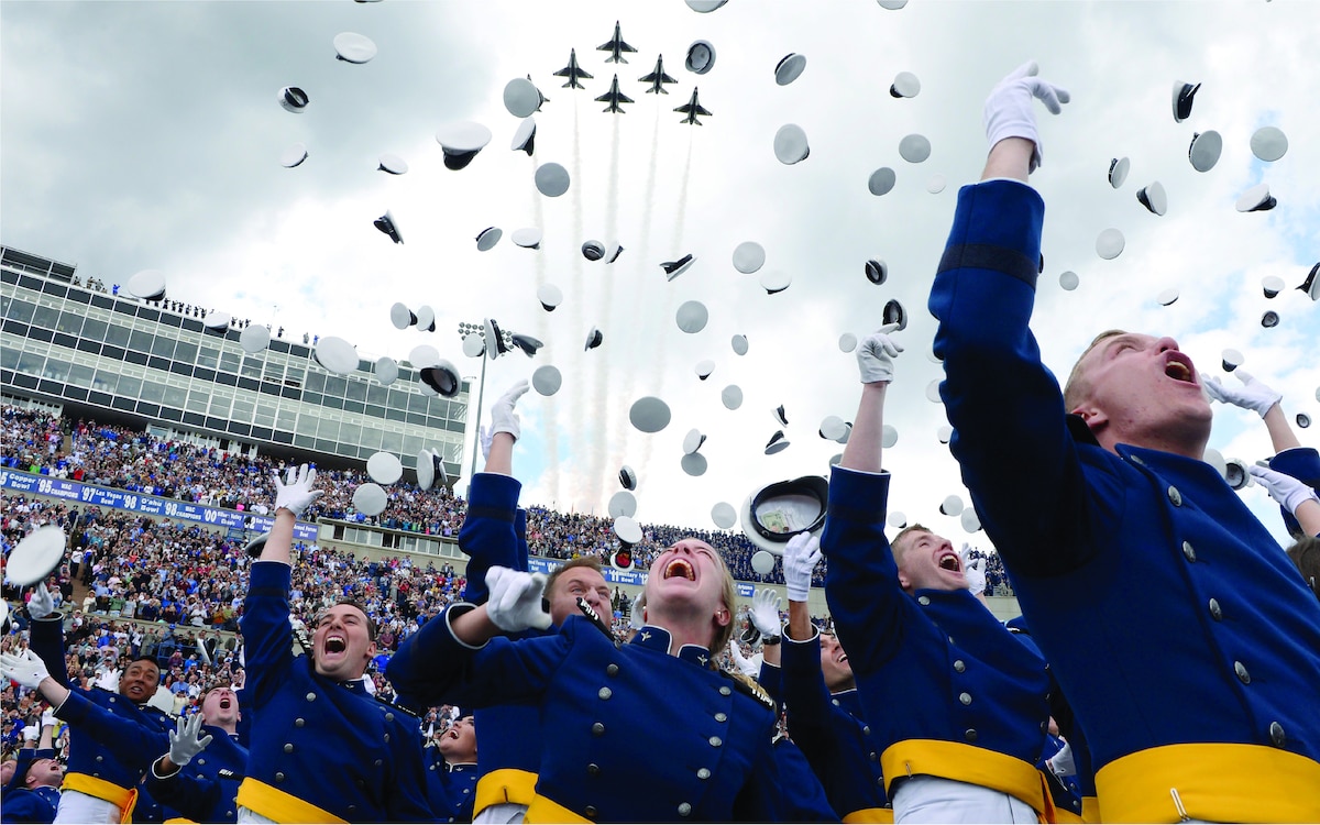 Group of cadets throwing their hats in the air at the end of a ceremony with fly by overhead