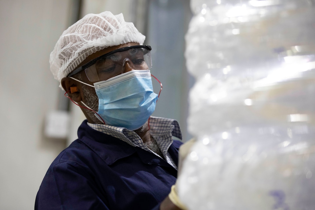 A government contractor wearing a face mask, protective eyewear and gloves marks a palate of packaged ice.