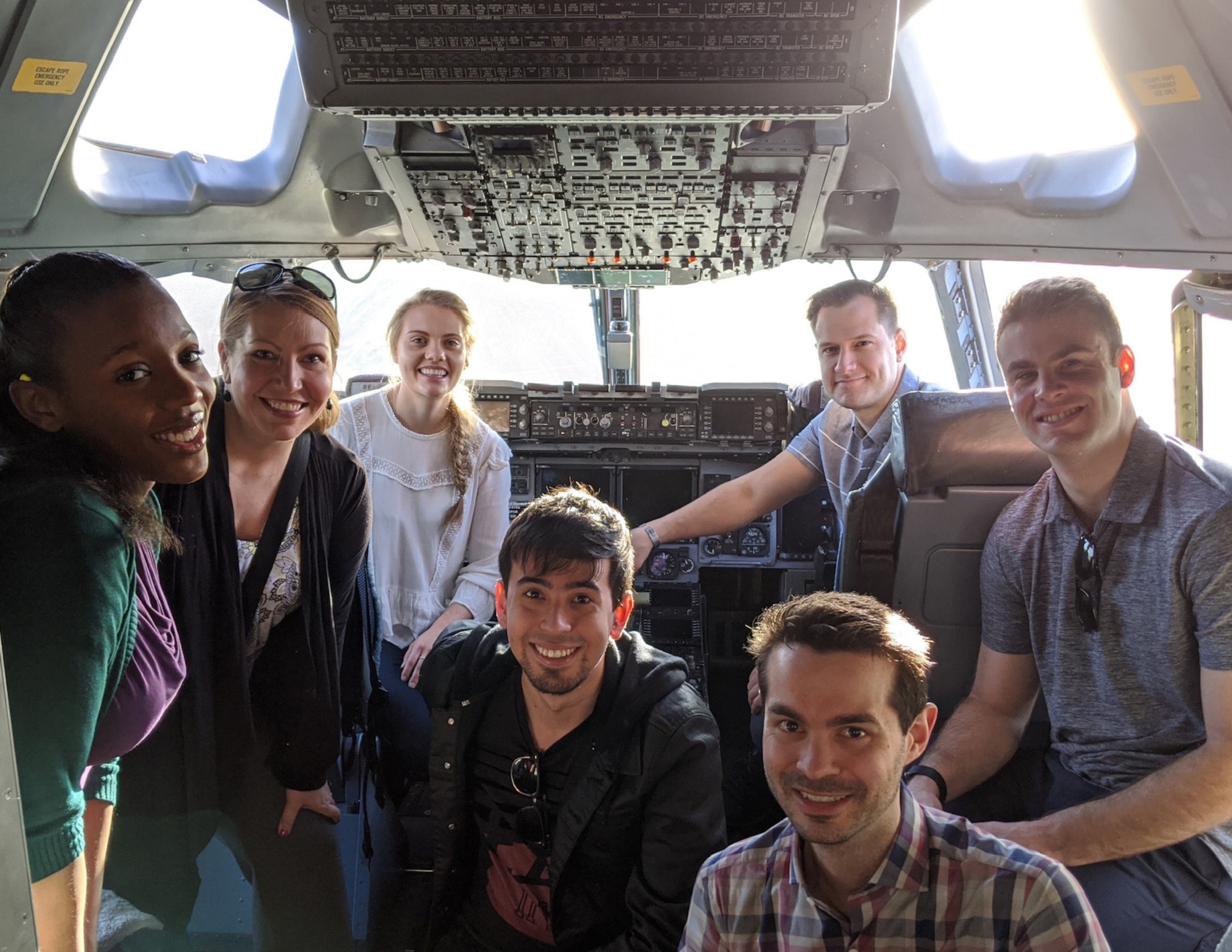 A team of civilians and Airmen researching artificial intelligence smiles in the cockpit of a C-17 Globemaster III.