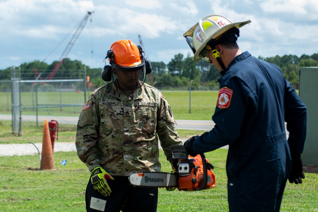 A firefighter shows a soldier how to hold a chainsaw.