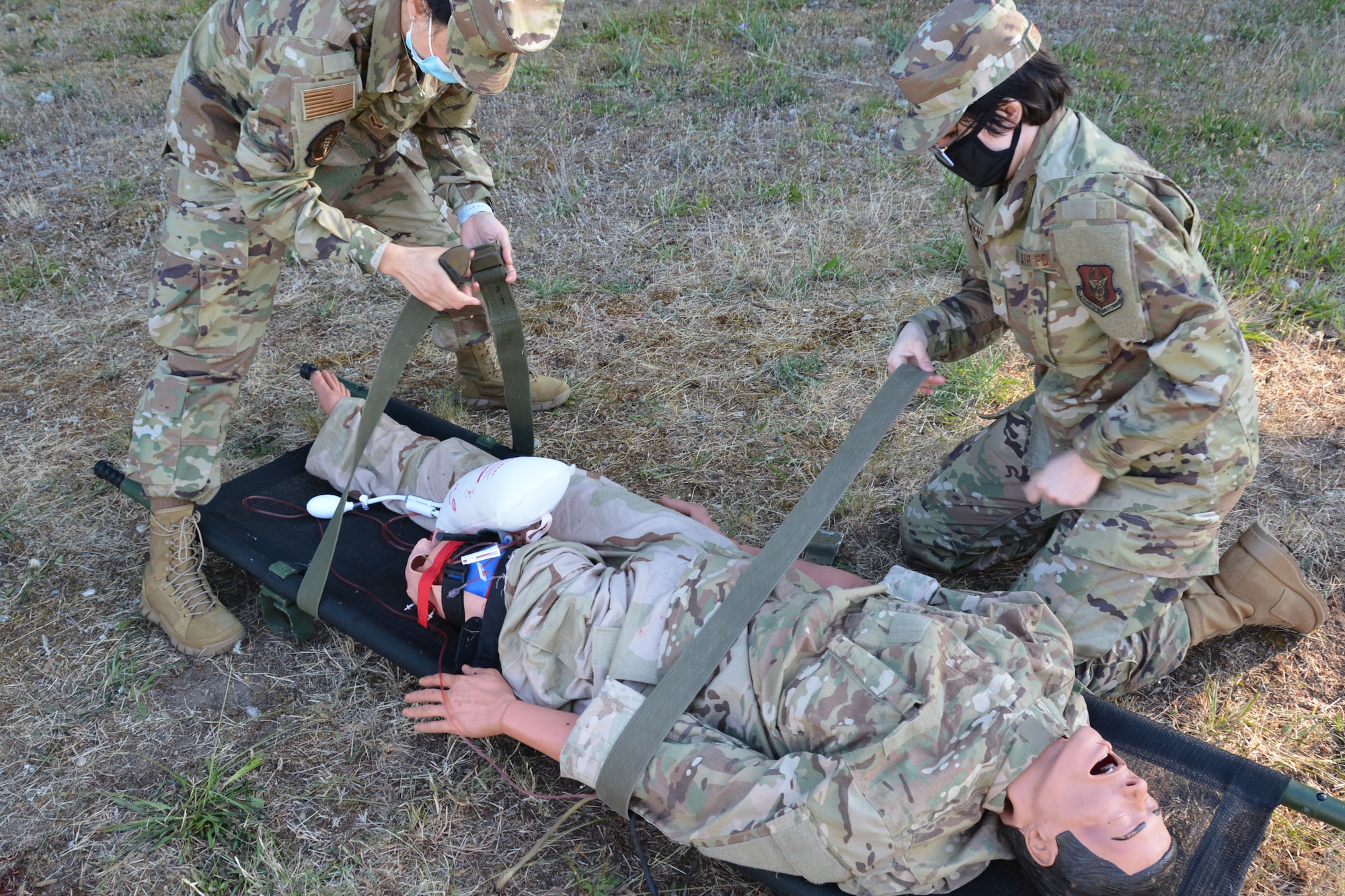 Two medics strap a mannequin to a litter