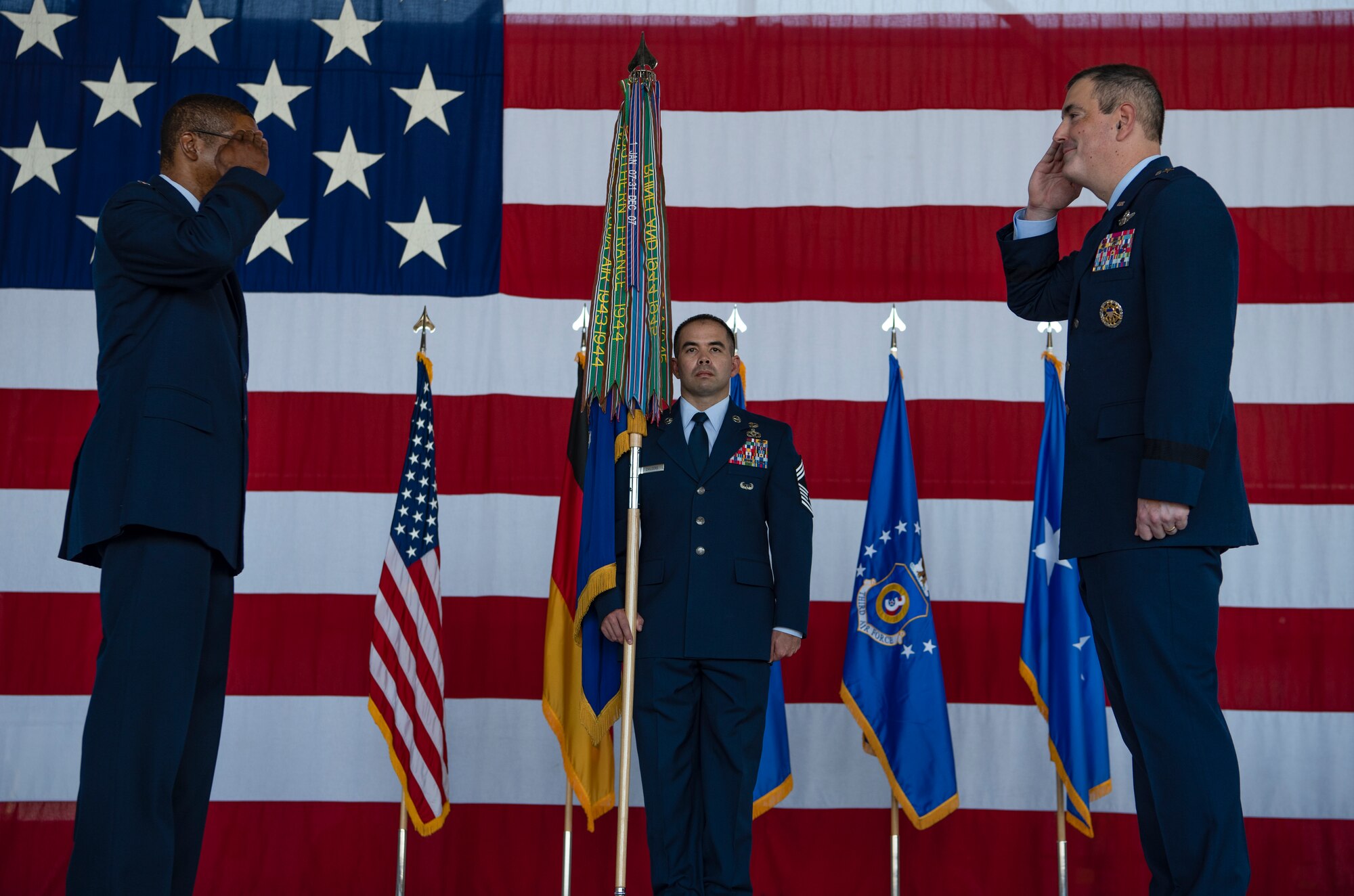 Two people saluting each other, while a third person is holding a guidon.