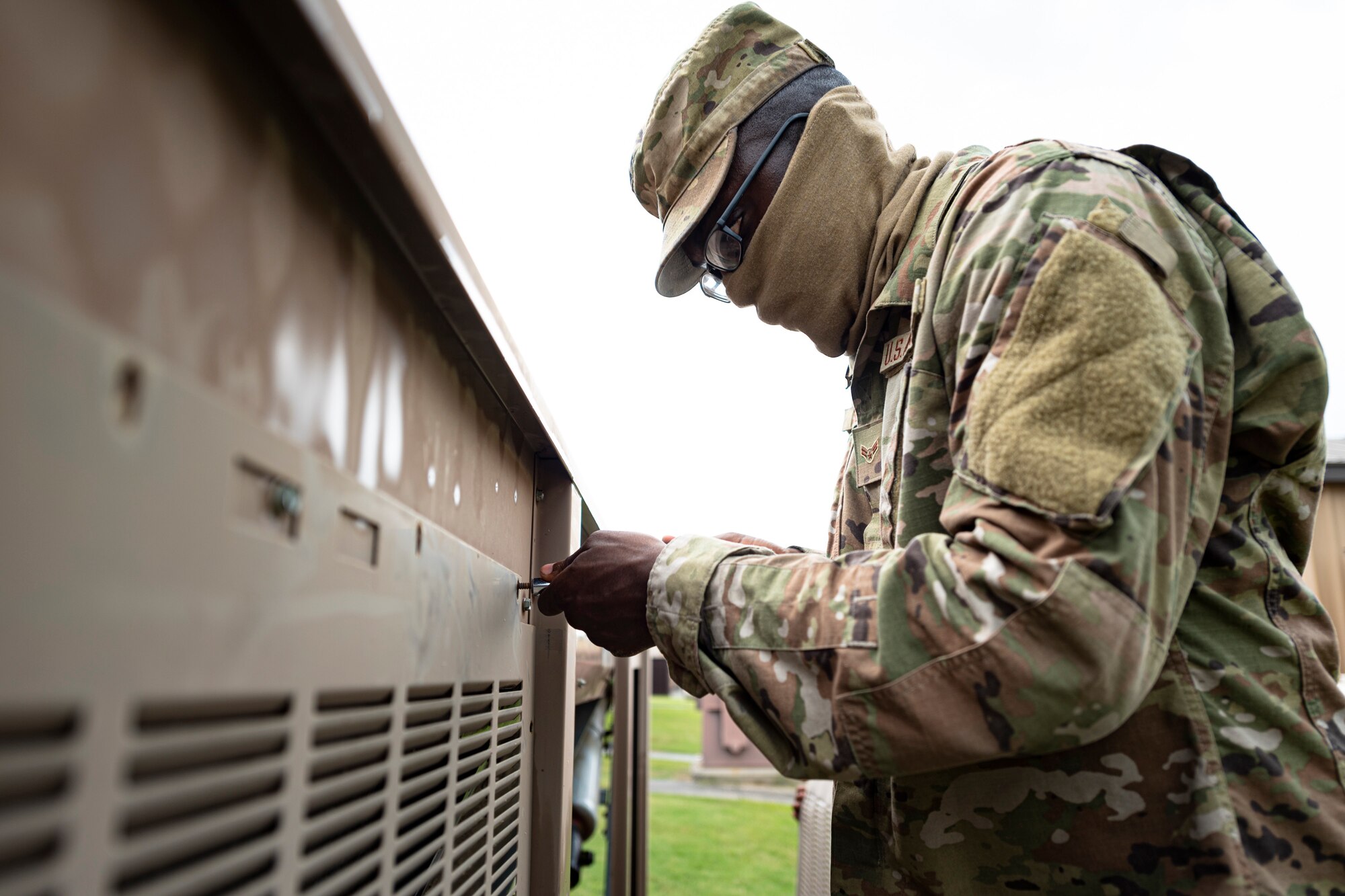 A photo of an Airman screwing a panel onto a condenser