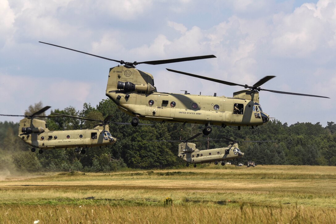 Three helicopters lift off from a field.