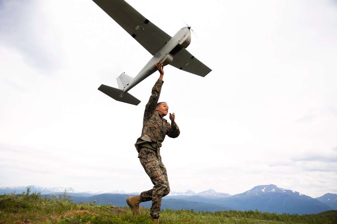 A Marine launches an unmanned aircraft with mountains in the background.