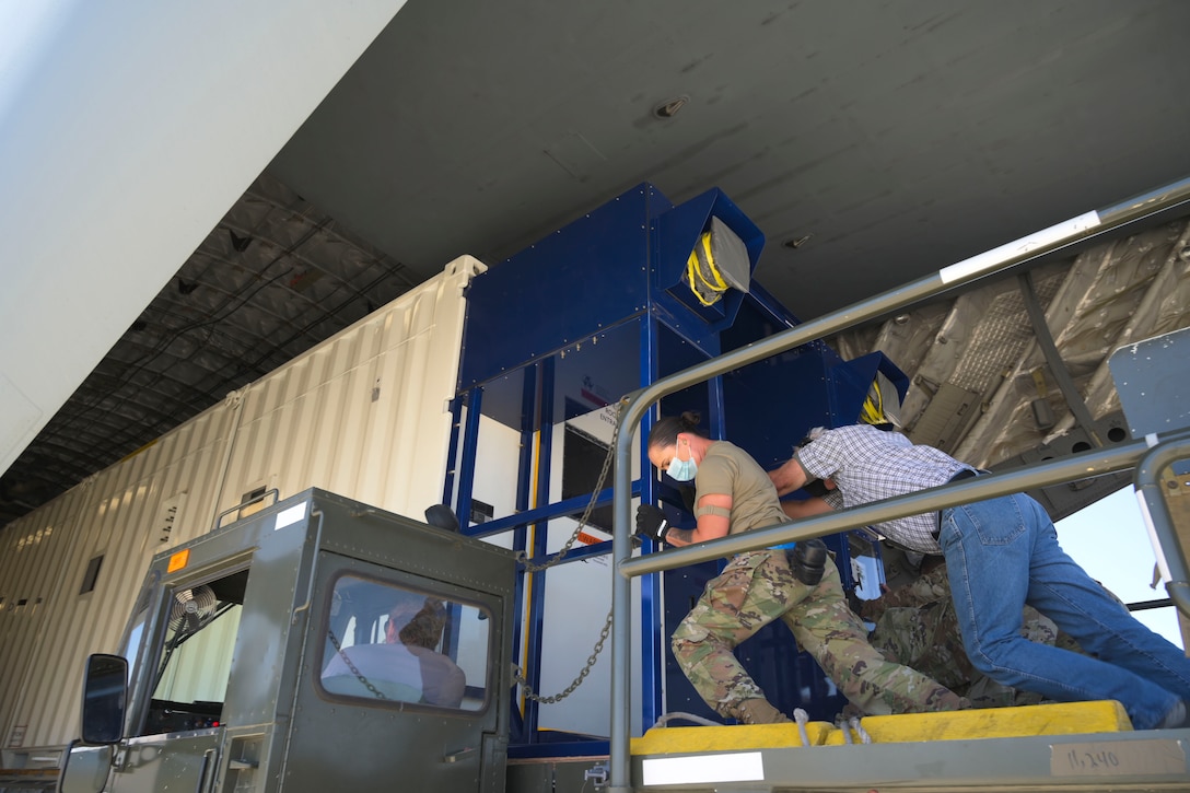 Airman and another man load equipment into a C-17 Globemaster III.