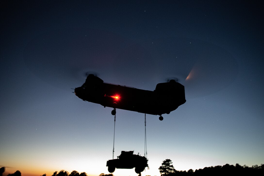 A helicopter lifts a vehicle at night.