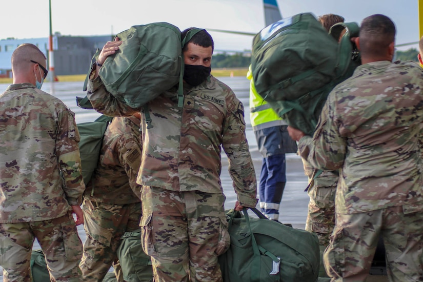 Soldiers wearing face masks retrieve their duffel bags upon arriving at their deployment location.