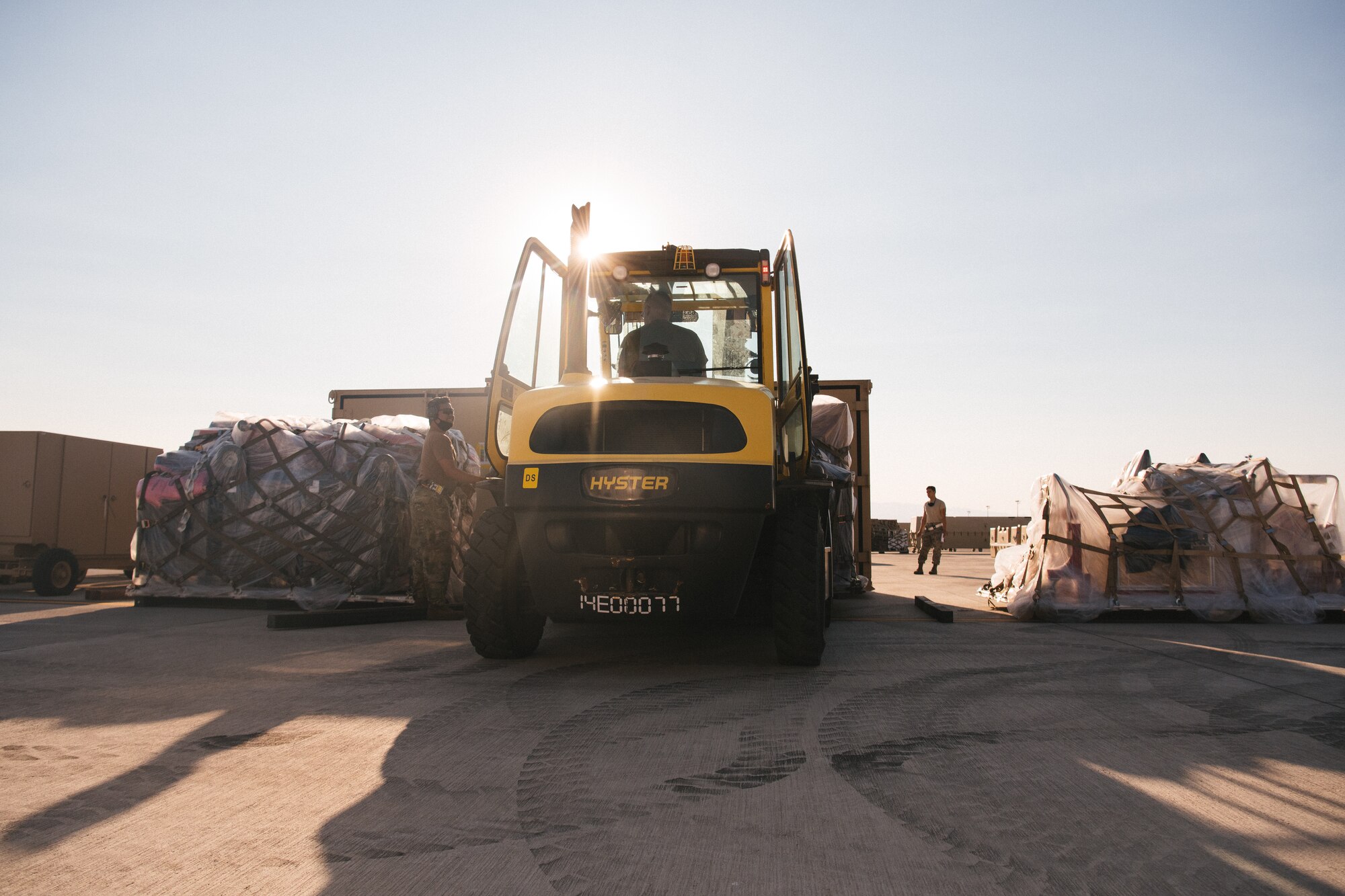 A yellow forklift moves equipment as an Airmen guides it.