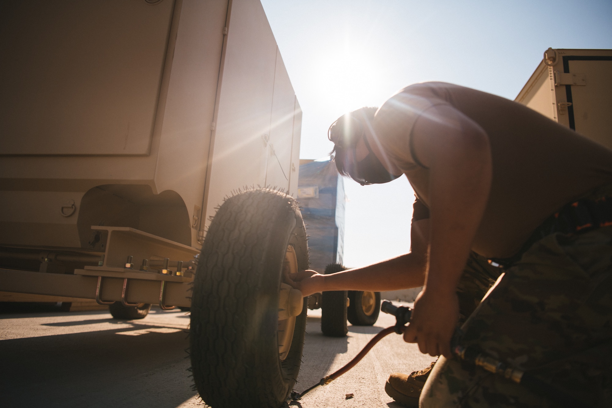 Senior Airman Orivin, 432nd Aircraft Maintenance Squadron weapons load crew member, is lit from the sun from behind as he fills a tire with air.