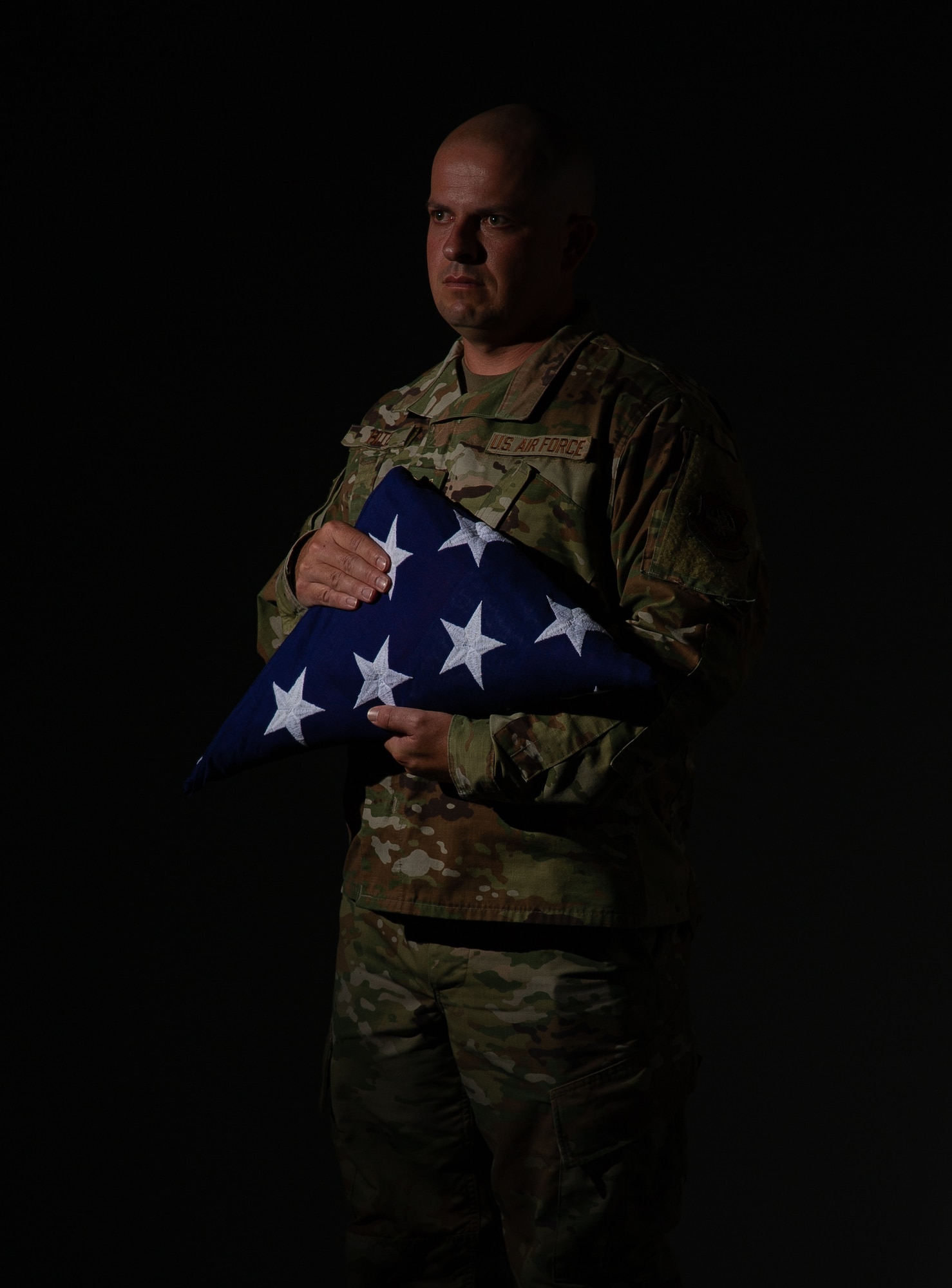 An airmen holds a flag in a dark studio.