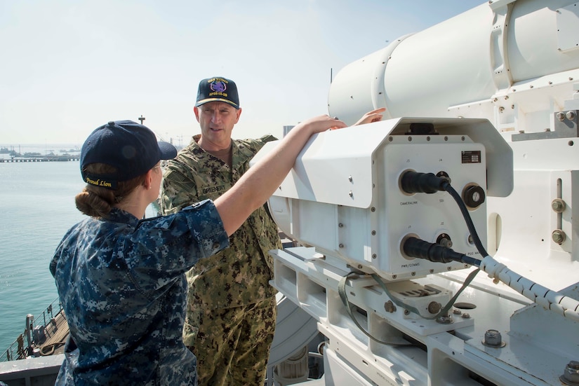 A man and a woman, both in uniform, stand near a laser system.