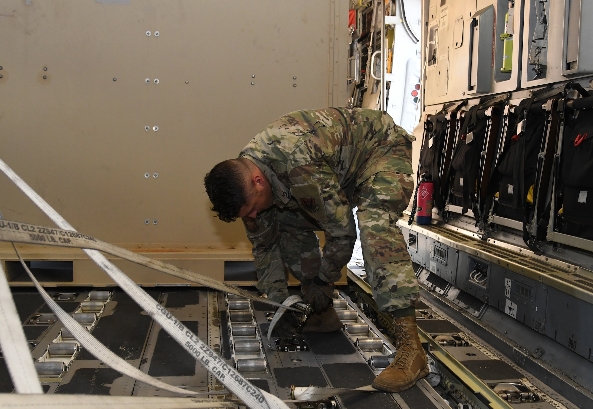An Airman unhooks cargo from the floor of a plane.