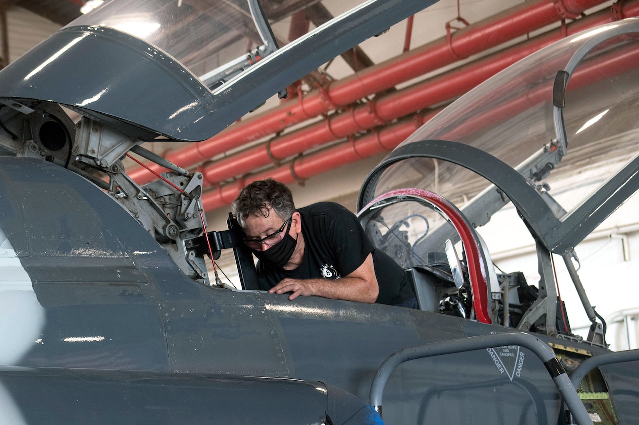 A man wearing a face mask repairs an aircraft seat.