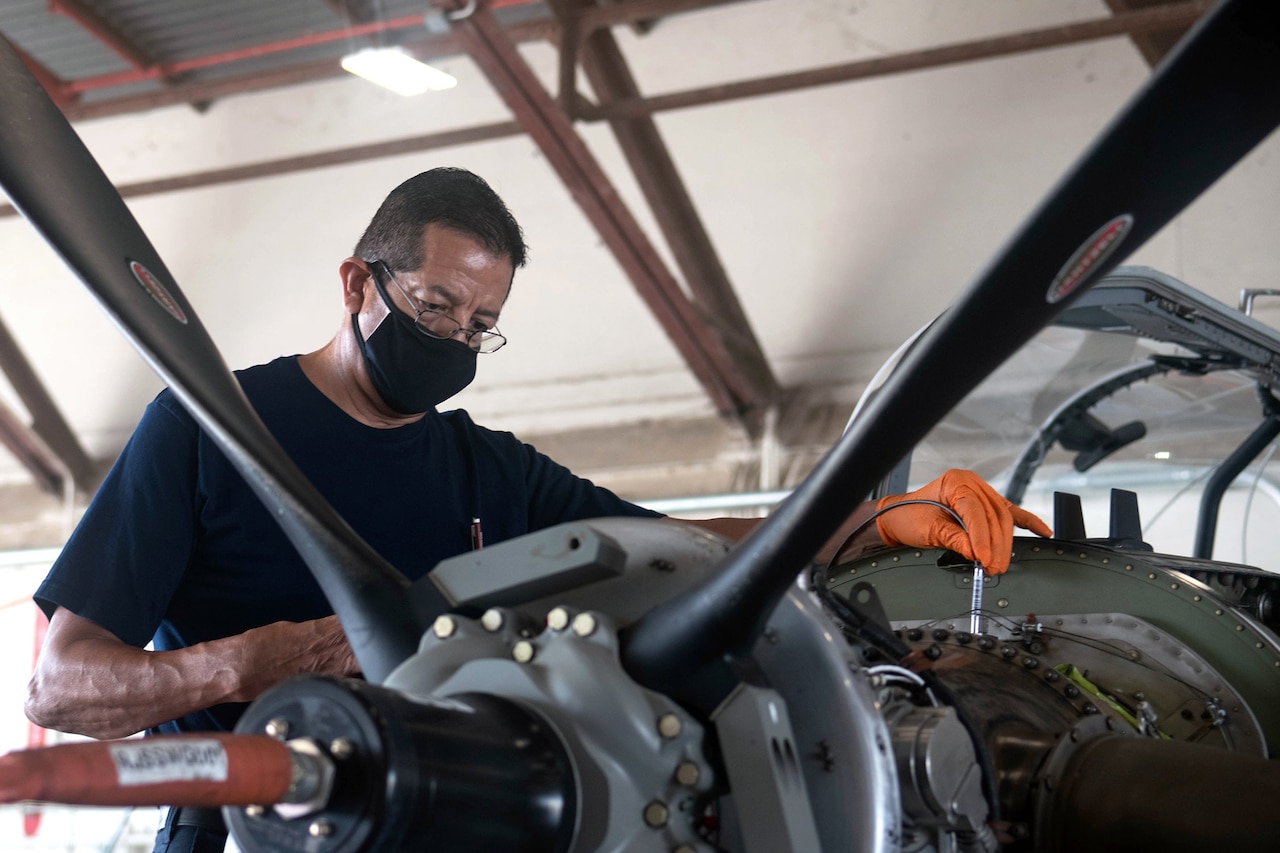 A man wearing a face mask checks an aircraft engine.
