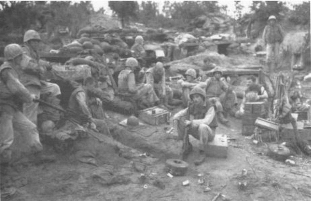 Several men in helmets sit around near a bunker.