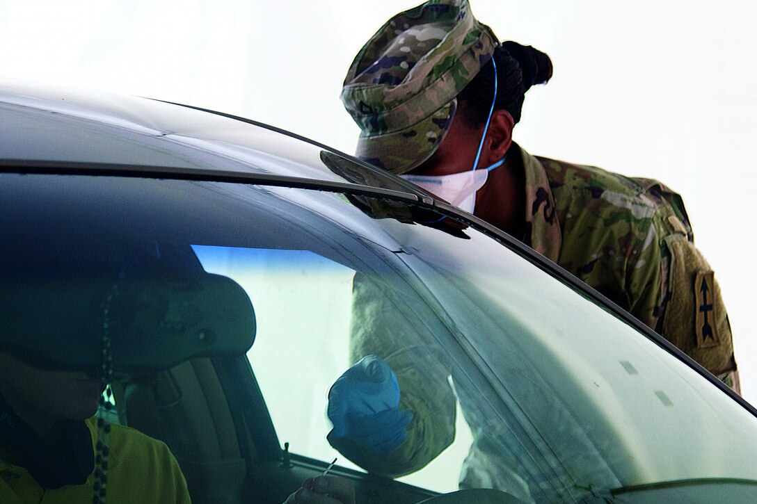 A soldier wearing a face mask and gloves administers COVID-19 testing for students and faculty.