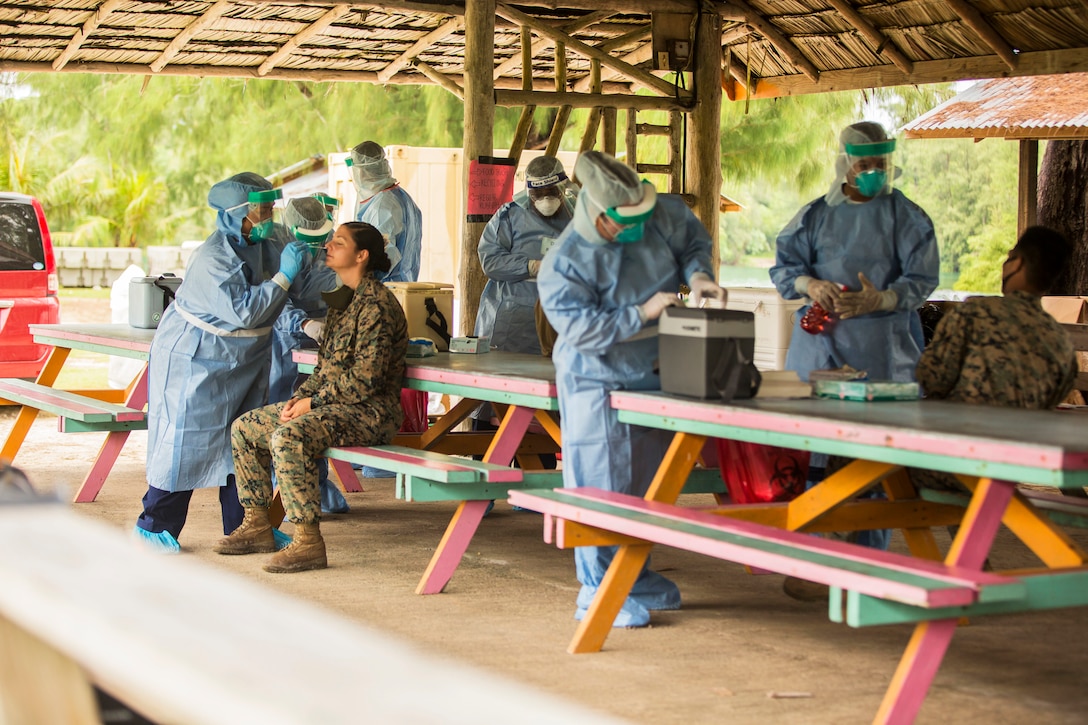 Several Marines and sailors wearing personal protective equipment provide COVID-19 testing.