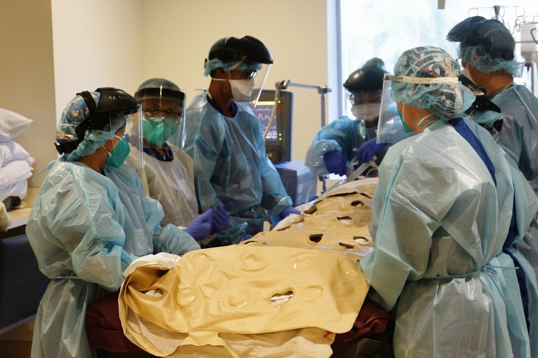 An Air Force Staff Sgt. and several civilian personnel, all wearing personal protective equipment, prepare to move a patient.