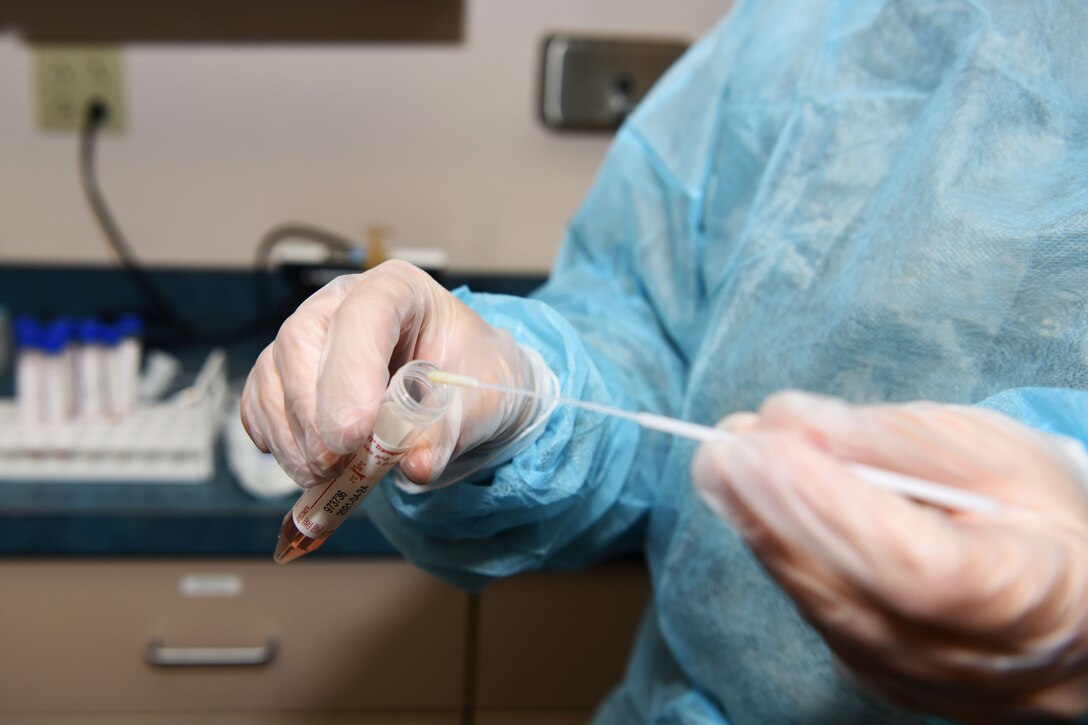 An airman wearing personal protective equipment prepares a nasopharyngeal swab test.