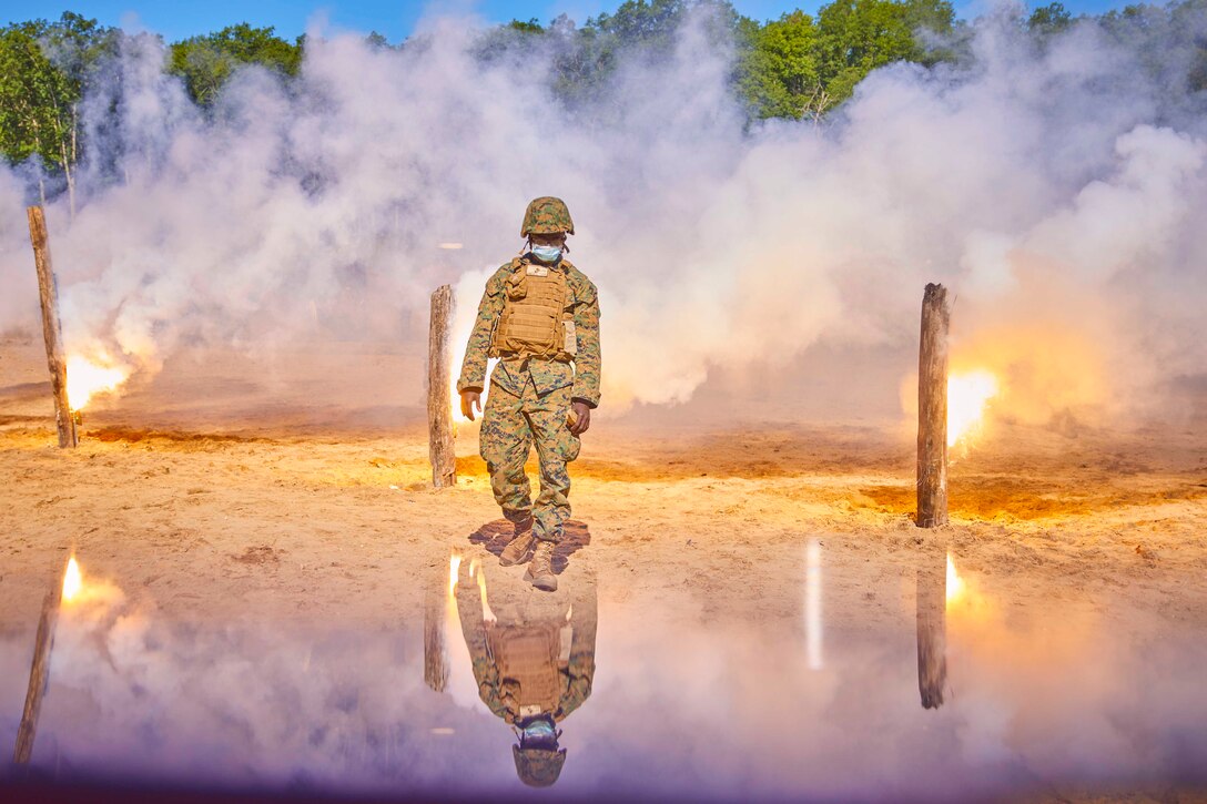 A sailor surrounded by smoke walks in between small fires.