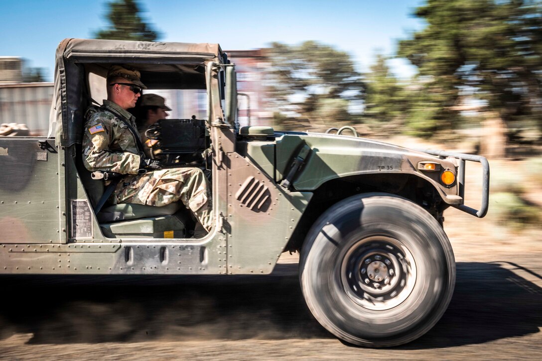 Two soldiers drive in a military vehicle.