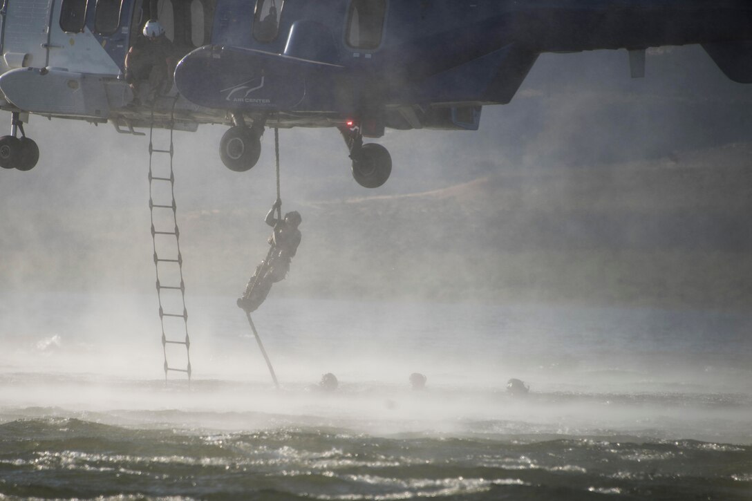 An airman rappels out of an aircraft over a lake.