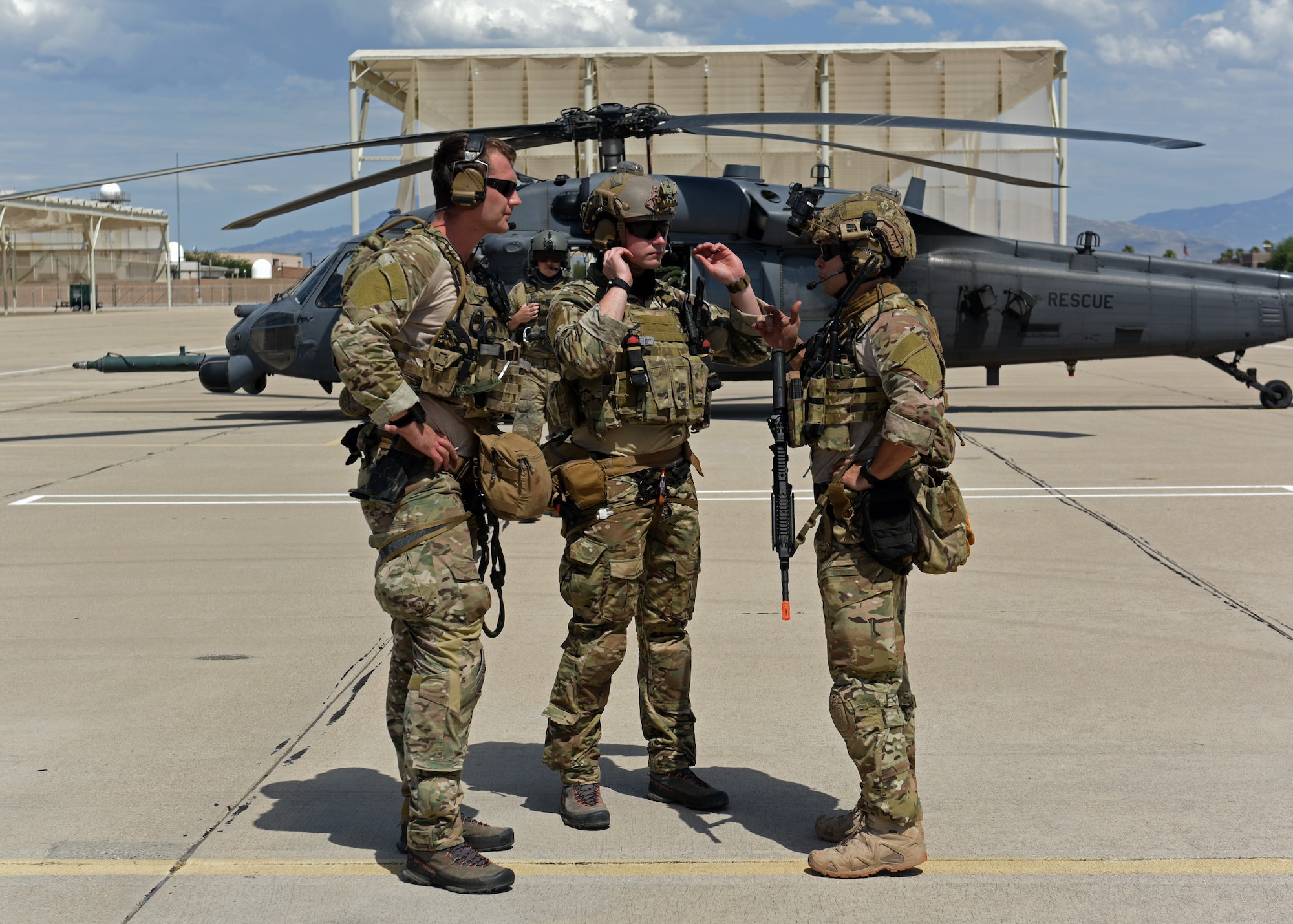 Photo of three Air Force Airmen talking in front of an HH-60G Pavehawk