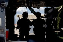 Photo of two Air Force Airmen casting a silhouette behind the side door of an HH-60G Pavehawk on a military flightline