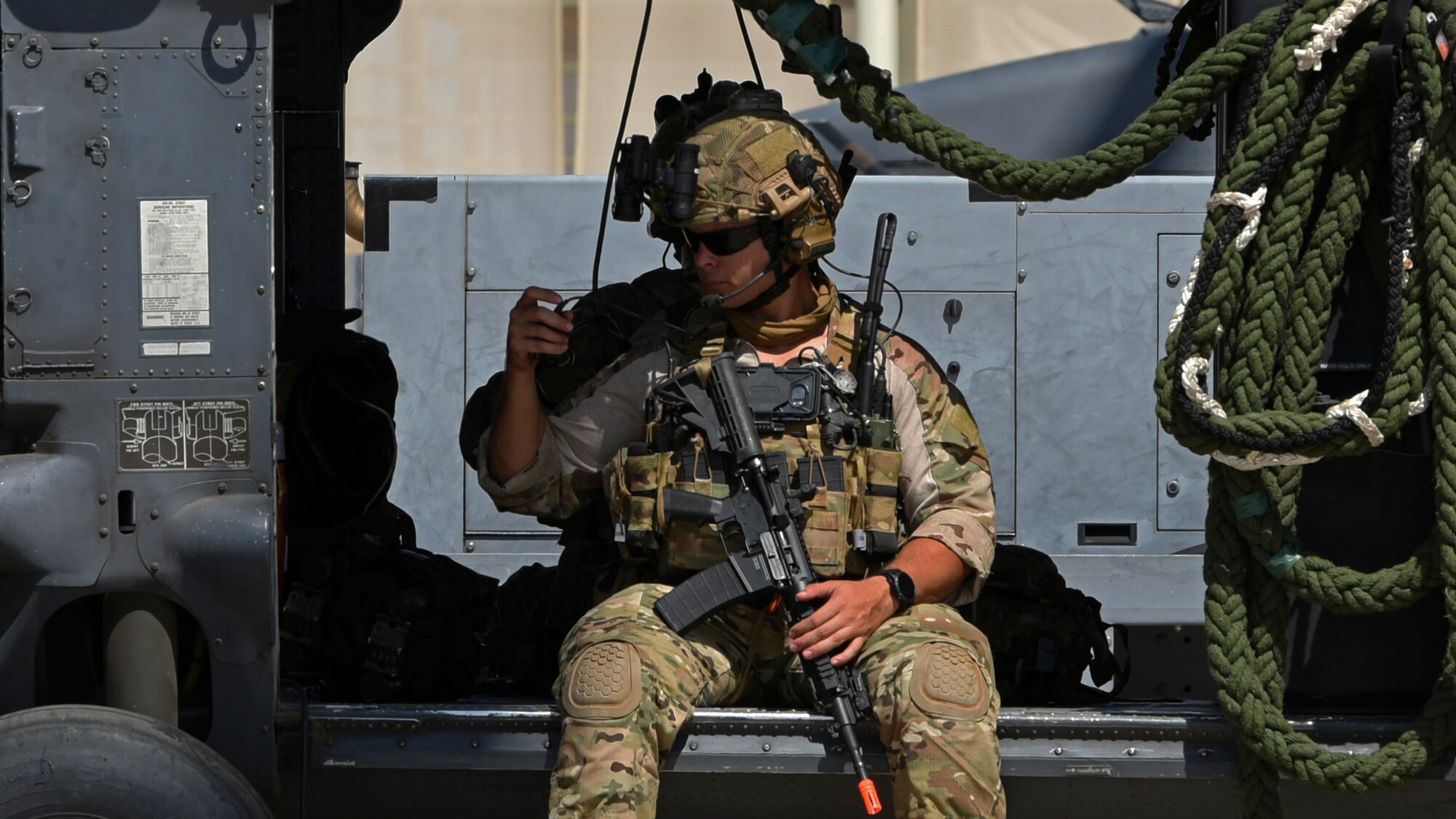 Photo of an Air Force Airman sitting and with his legs hanging off the side of an HH-60G Pavehawk