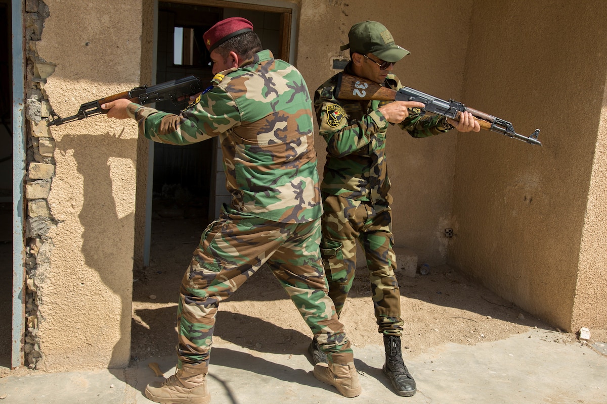 Two men in military uniforms face in the opposite direction and aim rifles.