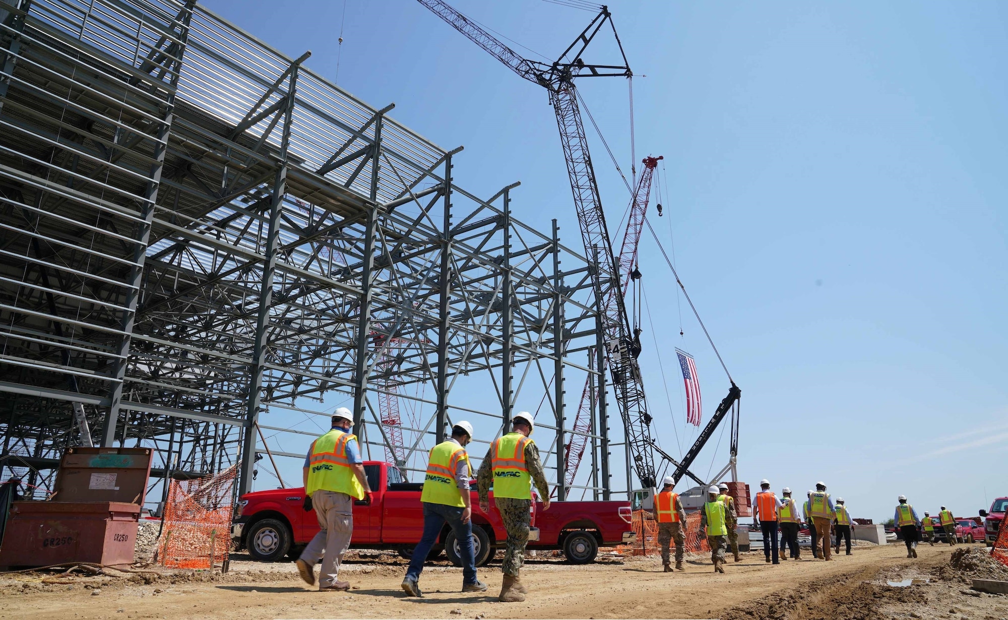 NAVFAC personnel walk around the steel frame of an aircraft hangar in construction.