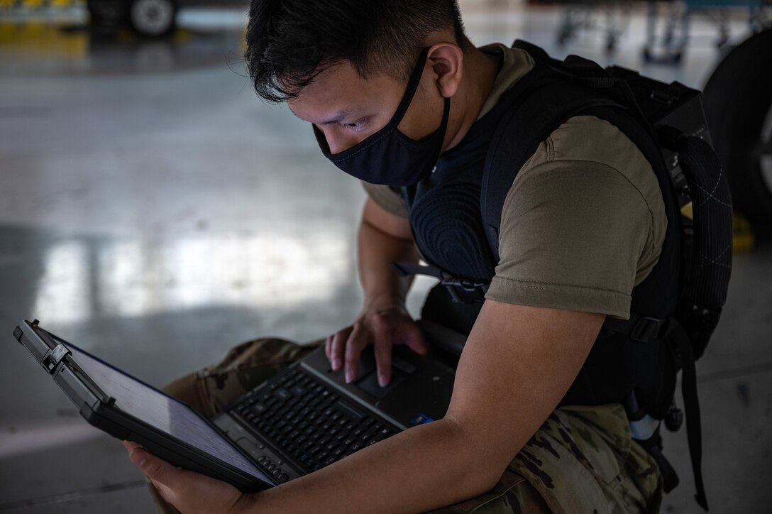 An Airman works on a laptop while under an F-22 Raptor.