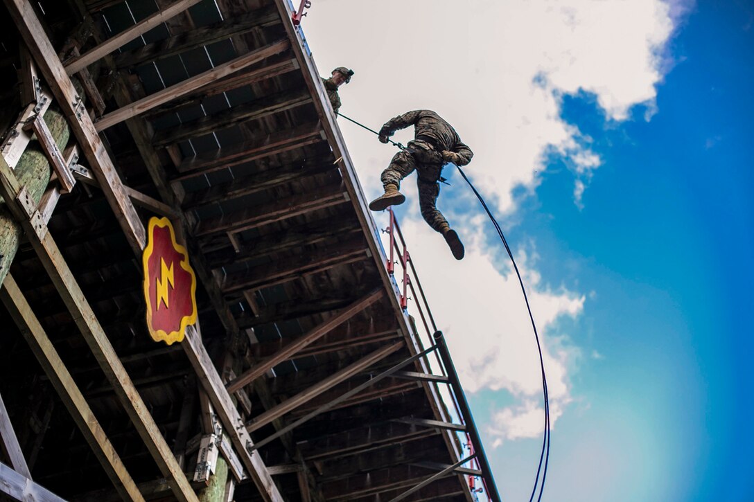 A Marine rappels from a skid as another Marine watches.